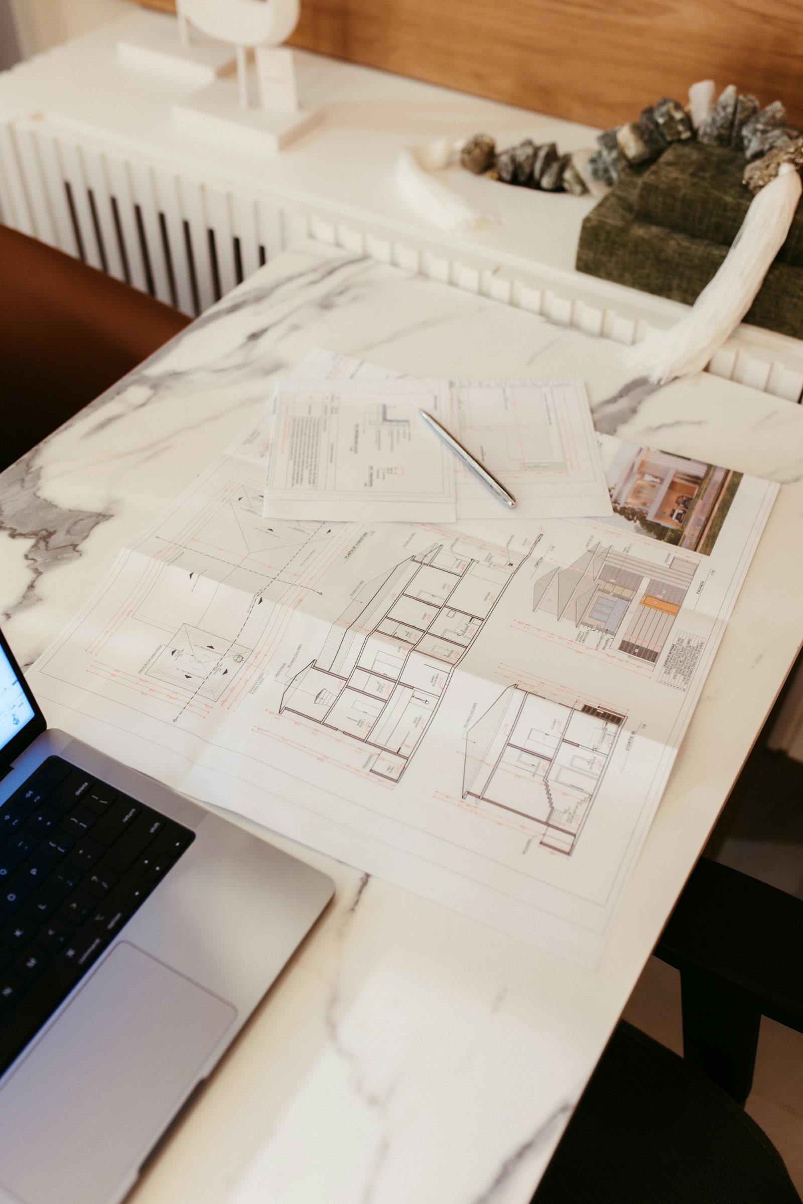 Planos de una casa sobre un escritorio junto a un computador